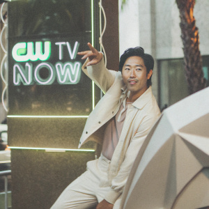 Aaron Yoo, Asian actor, dressed in a casual, stylish outfit. Poses against a dynamic, neon-lit backdrop with 'CW TV Now' logos. Friendly expression. Event setting.