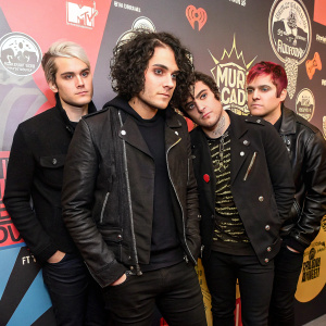 A candid shot of the My Chemical Romance band members: Mikey Way, Ray Toro, Frank Iero, and Gerard Way. Dark clothing, styled hair. Vibrant background with band logos.