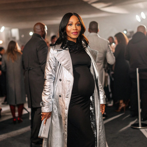 Jada Pinkett Smith at the Blockbuster Entertainment Awards. Pregnant and wearing a long metallic coat over a black dress. Crowded event, background filled with attendees.