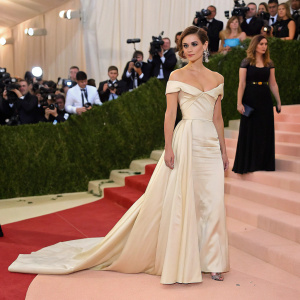Emma Watson at the Met Gala. Dressed in a stunning off-white gown. Crowded venue with guests taking photos on their smartphones.