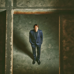 Antonio Conte, Chelsea FC manager, wearing a navy suit, standing alone in a empty, white room.