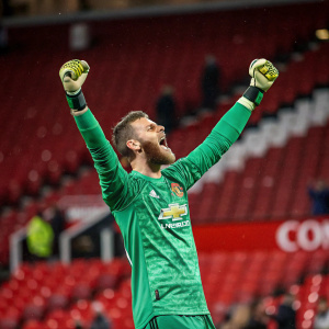 David De Gea, Manchester United goalkeeper, celebrating a save. Green jersey with sponsor logo. Stadium background, red seats