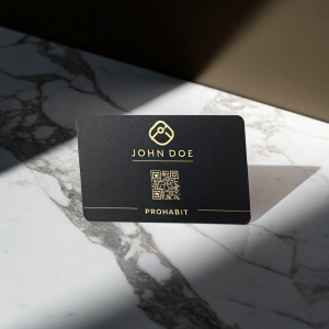 Business card for John Doe. Dark color scheme with ProHabit logo. QR code and contact info. Placed on a marble desk with dramatic lighting
