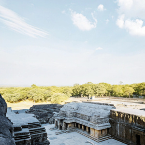 Aerial view of Kailasa Temple at Ellora Caves, carved from a single rock. Stone carvings depict scenes from Hindu epics. Weathered stone with lush greenery surrounding it.