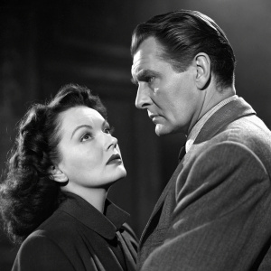 Linda Darnell and Jack Palance in a tense scene from 'Second Chance'. Linda Darnell has an intense expression, held by Jack Palance in a tailored suit. Dark, moody background highlighting their dramatic interaction.
