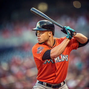 Giancarlo Stanton, in a intense batting stance, Miami Marlins jersey. Focused expression. Crowded stadium blurred in background.