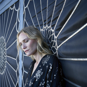Diane Kruger, blonde hair, deep in thought. Black dress with silver sequins. Blue backdrop with geometric patterns.