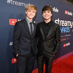 Sam Golbach and Colby Brock at the Streamy Awards. Sam in a dark suit with a matching tie, Colby in a sleek black tuxedo. Both on red carpet, dark blue backdrop with award logos