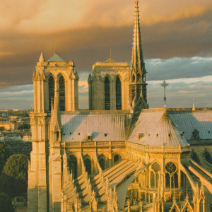 Aerial view of Notre-Dame Cathedral in Paris. Golden hour lighting, clouds casting shadows on the ancient stone structure.