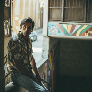 Chris Pine, starring at the camera with intense eyes. In casual jeans and a patterned shirt, against a vibrant street art backdrop.