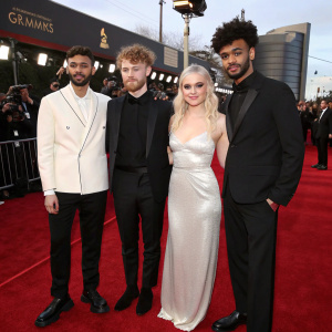 Jack Patterson, Luke Patterson, Grace Chatto, and Milan Neil Amin-Smith from Clean Bandit at the Grammy Awards. They're dressed in formal wear, standing on a red carpet.