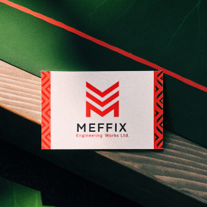 Professional business card for Meffix Engineering Works Ltd. Bold geometric M logo. White background with red accents. Contact information clearly displayed on a sleek wooden surface.