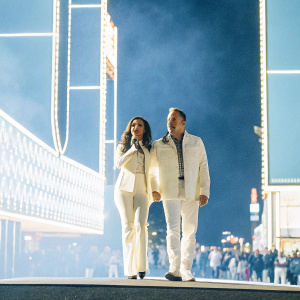 Karla Martinez and Alan Tacher at the Latin Grammy Awards. Neon lights and bustling crowd in the background, capturing the lively atmosphere of Las Vegas.