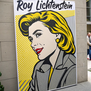 Roy Lichtenstein inspired artwork featuring a vibrant woman's portrait in a modern comic style. The illustration includes bold lines and uses yellow, black, and gray tones. Spanish text surrounds the image.