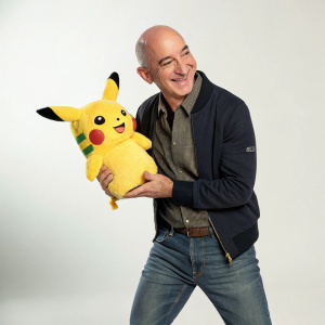 Jeff Bezos, in a casual outfit, interacting with Pikachu doll. Simple studio setup.