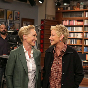 Anne Heche and Ellen DeGeneres on the set of a talk show. Bookshelf backdrop. Other crew members visible in background.
