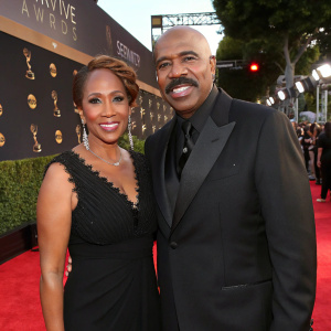 Steve Harvey and Marjorie Bridges at the Daytime Emmy Awards. Formal black suit and black dress. Red carpet ambiance.