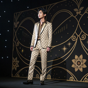 Yoo Seung-Ho, Asian actor, at a fashion gala. Black background with intricate golden patterns, spotlight illuminates his Gucci suit.