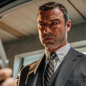 Close-up shot of Liev Schreiber. Dark suit and tie. Serious expression. Studio lighting setup
