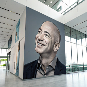Digital illustration of Jeff Bezos' smiling face overlaid on a sleek modern office wall.