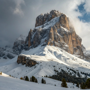 A majestic snowy peak in the Dolomite Alps, located in Canazei, Val di Fassa, Trentino-Alto-Adige, Italy. Rock faces peek through the thick blanket of snow, creating a striking contrast of brown and white.