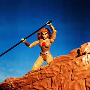 Cheetara from Thundercats figurine in dramatic pose, wielding a black staff. Her costume features intricate mesh design with a red emblem. Set against stark black backdrop.