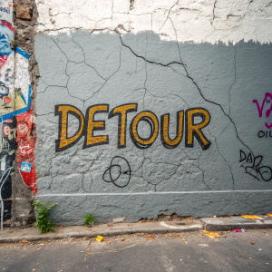 Textured gray wall with graffiti art. The word 'Detour' is painted in bold, industrial font at the center.