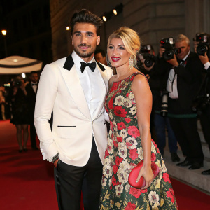 Mariano Di Vaio and Hofit Golan at an exclusive Fendi fashion gala. Mariano in a sleek white tuxedo, Hofit in a vibrant floral gown. Red carpet with flashing cameras