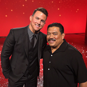 Channing Tatum at Jimmy Kimmel Live. Hispanic Guillermo Rodriguez stands beside him. Channing wears a black suit. Bright red background with sparkling floor.