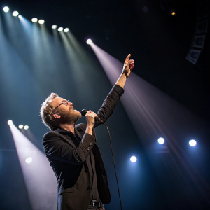 Matt Berninger, singer, performing intense setlist. Bright stage lights, audience not visible, dark backdrop