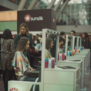 3D model of Sunsilk booth at beauty expo. Vibrant, eye-catching design with Sunsilk branding. Interactive hair styling stations, models showcasing new products. Background filled with engaged attendees