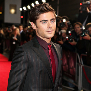 Zac Efron at a high-profile awards ceremony, wearing a sleek black suit with a subtle pinstripe pattern, paired with a burgundy silk tie. Crowd and flashes in background