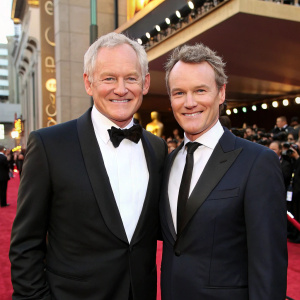 Victor Garber and Tate Donovan, in suits, at the Academy Awards. Smiling for the cameras. Red carpet backdrop.