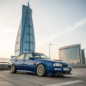 A Blue Ford Sierra Sapphire RS Cosworth parked in front of a sleek, contemporary skyscraper. The car stands out in the foreground, showcasing its unique design and features.