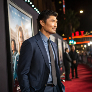 Rick Yune, dressed in a tailored suit, at the film festival premiere. Subtle smile, standing in front of the movie poster.