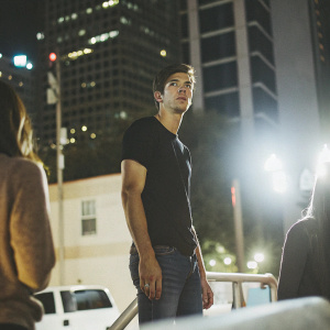 Grant Gustin, intense gaze, in a casual setting. Black t-shirt and jeans. Brightly lit, urban backdrop.