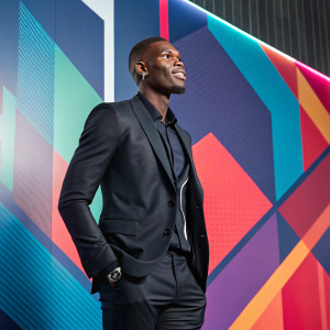 Paul Pogba in a sleek business suit, posing in front of an abstract digital art backdrop.