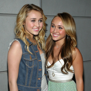 Miley Cyrus and Hayden Panettiere, young actresses, pose for candid shot at charity gala. Gray backdrop, casual outfits, friendly interaction