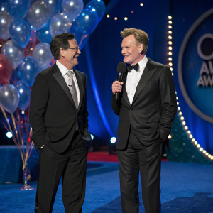 Stephen Colbert and Conan O'Brien at Comedy Central Awards. Both are standing on a blue carpeted stage with balloons and streamers in the background.