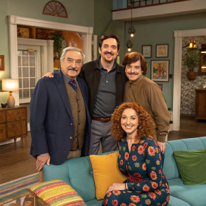 A group photo from the set of 'Mr. Belvedere', featuring a cozy living room scene with classic decor. Cast includes an older gentleman, another with a mustache, a younger man, and a woman with curly reddish-brown hair. The setting is now a vibrant, modern home interior.