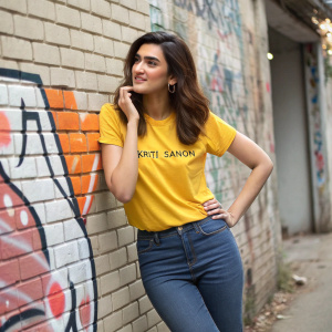 Kriti Sanon, south asian actress, in casual attire. Wearing a yellow t-shirt with slogan. Standing in front of a graffiti-covered brick wall