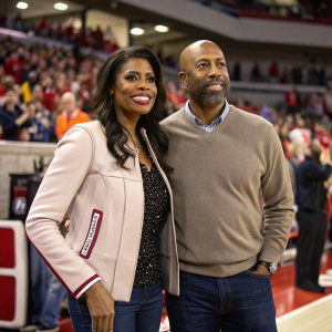 Omarosa Manigault-Stallworth and Kenny Smith on the sidelines of a sports event. Both dressed casually. Crowd cheering in the background.