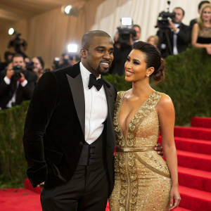 Kanye West and Kim Kardashian celebrating at the Met Gala. Black tuxedo, gold dress, red carpet backdrop.