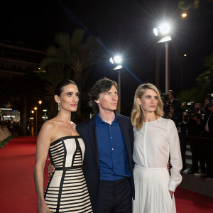 Jennifer Connelly, Cillian Murphy, and Melanie Laurent at the Cannes Film Festival premiere. Jennifer in black and white halter-neck dress. Cillian in blue shirt. Melanie in white blouse. Nighttime, spotlights.