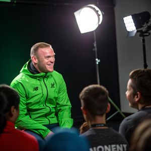 Wayne Rooney, soccer legend, wearing a vibrant green jacket. In a Q&A session with fans, bright studio lights