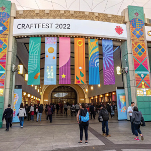 The grand entrance of CraftFest 2022. A vibrant array of banners and info panels guiding visitors. A bustling crowd around the entrance.
