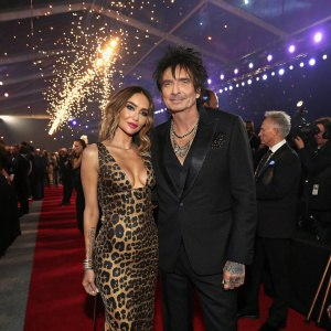Tommy Lee and Sofia Toufa at a glamorous award show. Both are dressed in designer attire. Sofia in a sleek leopard print dress, Tommy in a tailored black suit. Crowded event space with sparkling lights and paparazzi.