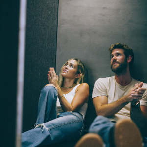 Miley Cyrus and Liam Hemsworth in a candid shot. Grey backdrop
