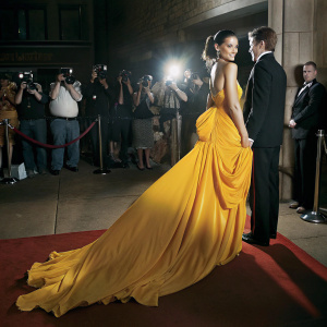 Katie Holmes in a stunning white gown and James Van Der Beek in a black tuxedo at a bustling gala event. Red carpet surrounded by photographers and fans.