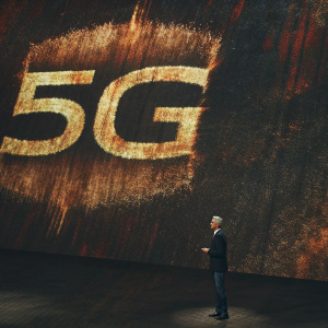 Tim Cook, CEO of Apple, at the 5G product launch. He stands in front of a huge digital screen displaying the 5G logo in vibrant colors against a black backdrop.